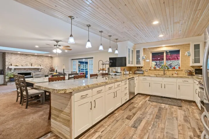 Kitchen with a peninsula, a fireplace, white cabinetry, crown molding, and wood ceiling