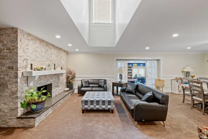 Living room featuring a wainscoted wall, a stone fireplace, carpet floors, recessed lighting, and a decorative wall