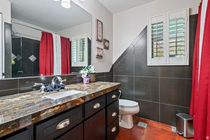 Full bath featuring tile walls, vanity, dark tile patterned flooring, and curtained shower