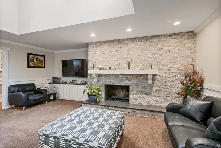Carpeted living room featuring ornamental molding, a stone fireplace, and recessed lighting