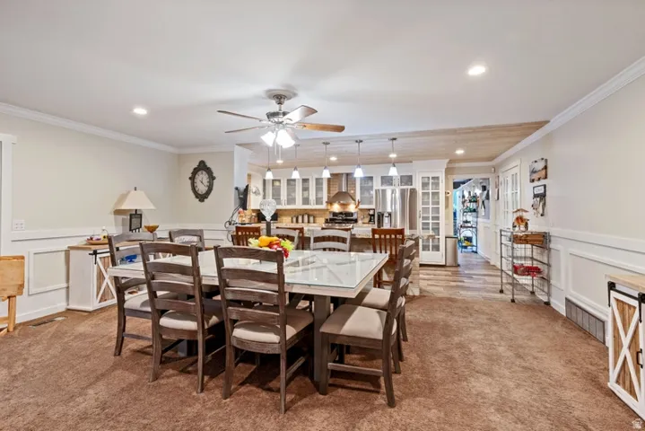 Dining room featuring a decorative wall, wainscoting, light carpet, a ceiling fan, and crown molding