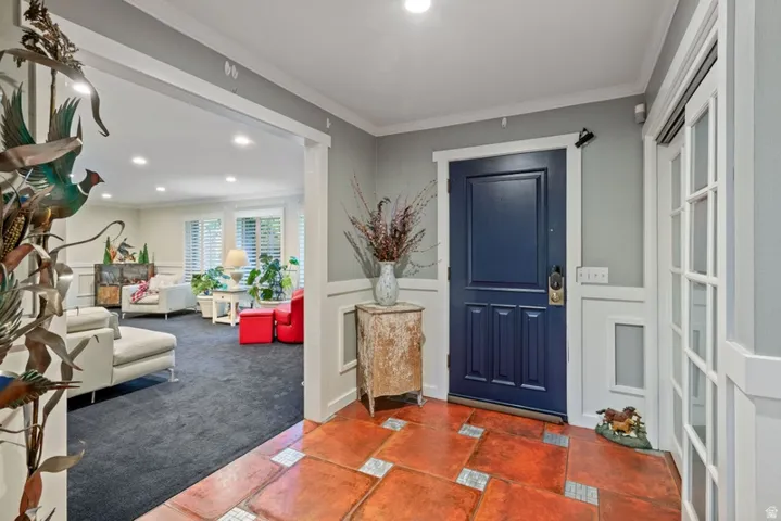 Carpeted foyer featuring ornamental molding, a decorative wall, wainscoting, recessed lighting, and tile patterned flooring