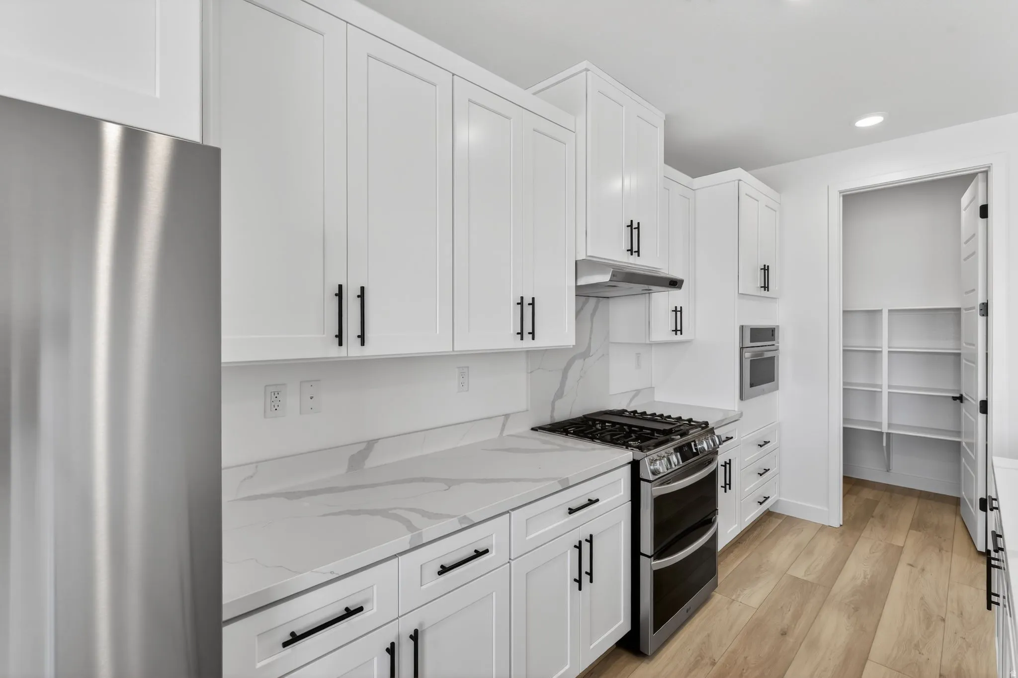 Kitchen featuring stainless steel appliances, light wood-style floors, white cabinetry, light stone counters, and recessed lighting