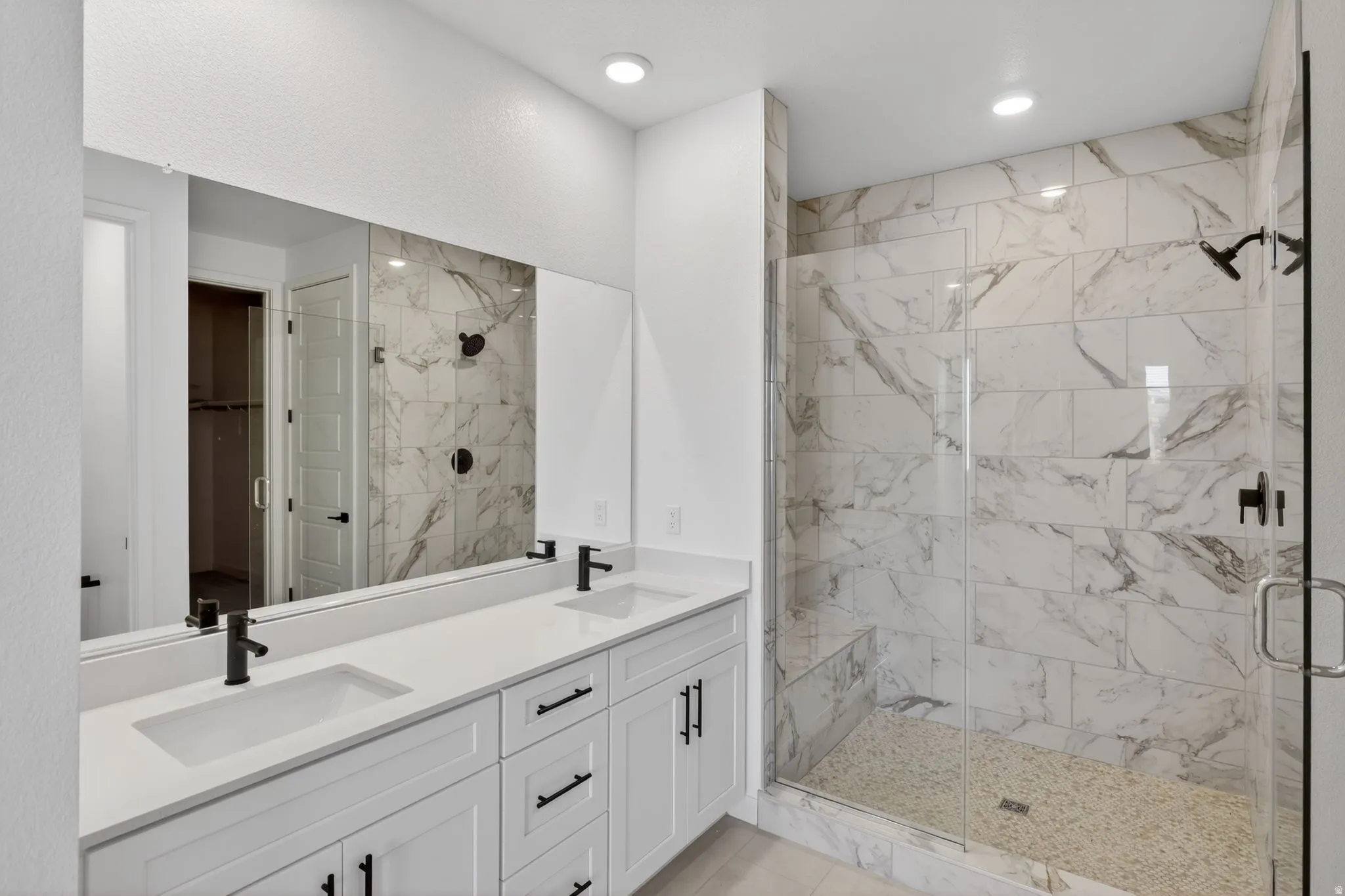 Bathroom featuring double vanity, a marble finish shower, a spacious closet, and recessed lighting