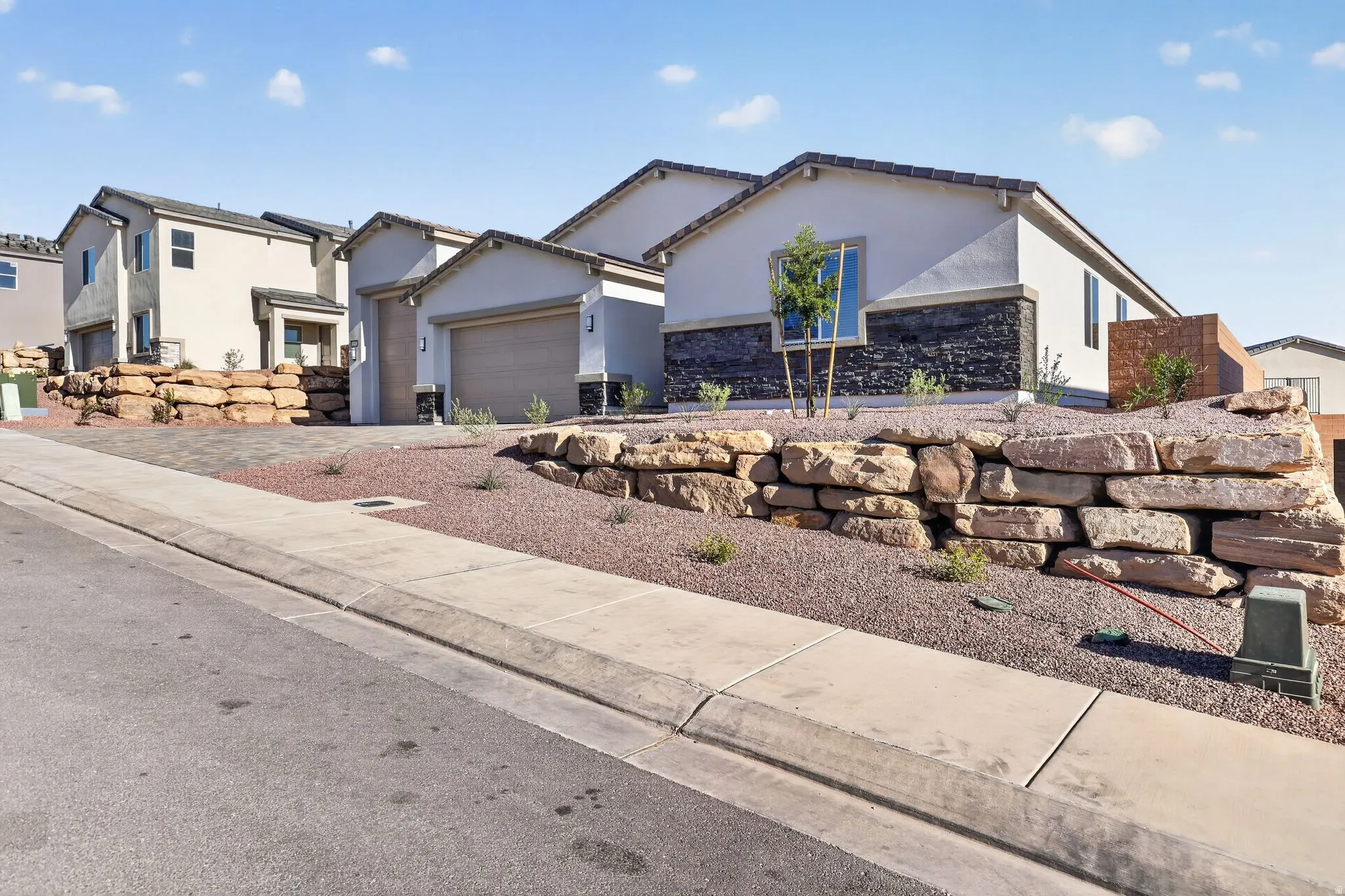 View of front facade with stucco siding, stone siding, an attached garage, and driveway