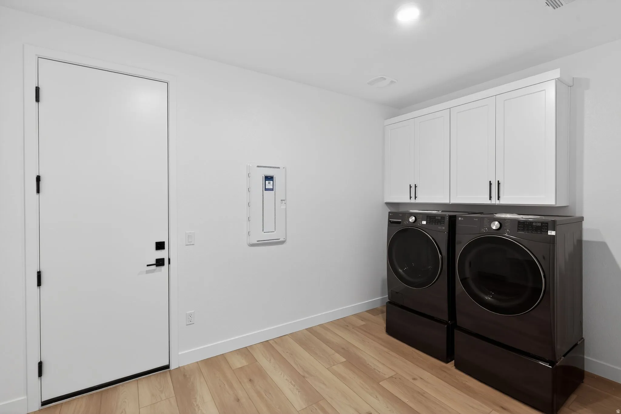 Laundry room featuring cabinet space, light wood-style floors, washing machine and clothes dryer, and electric panel