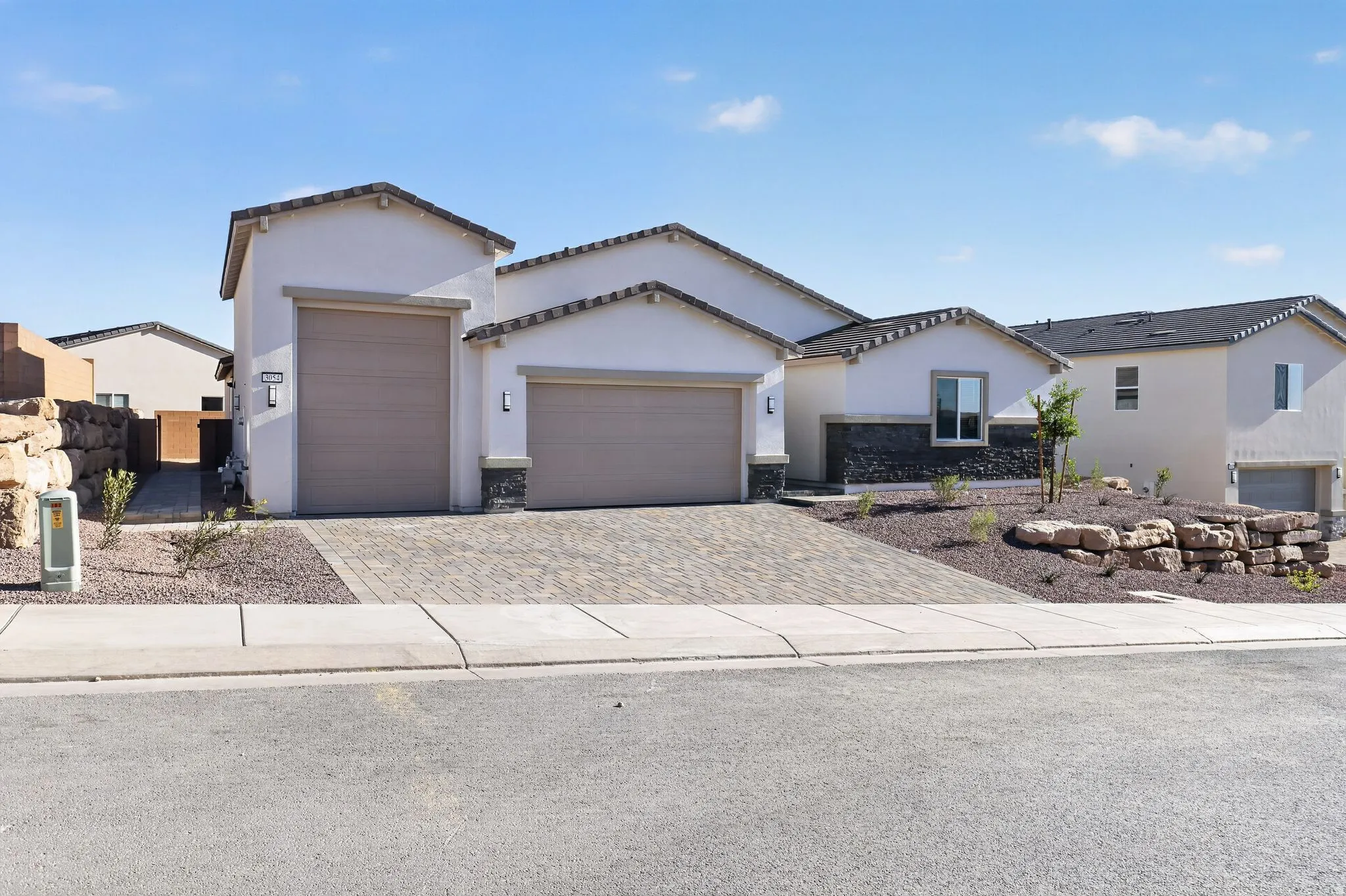 View of front of property featuring a garage, driveway, stucco siding, stone siding, and a tiled roof
