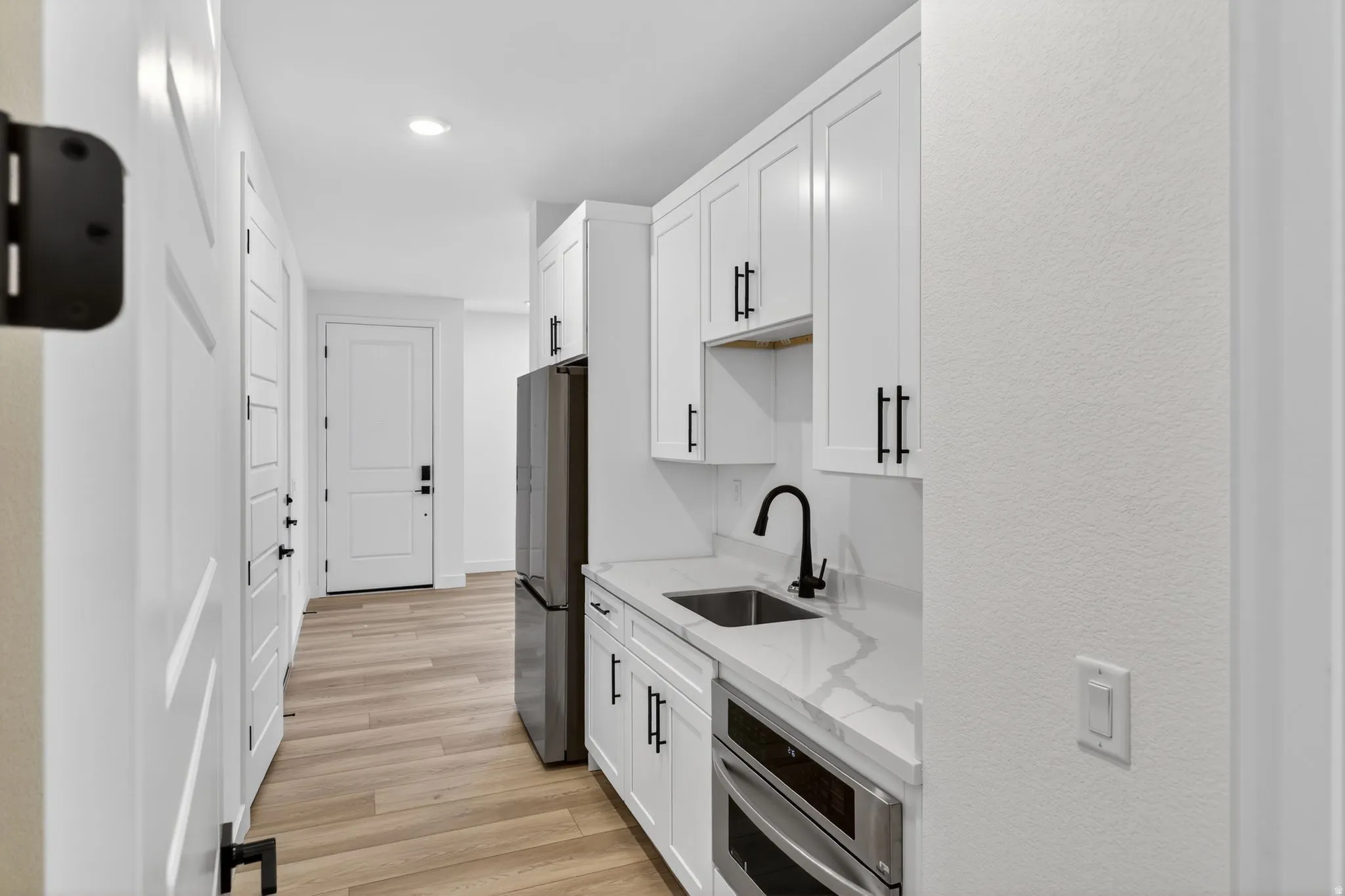 Kitchen featuring stainless steel appliances, white cabinets, light wood finished floors, light stone counters, and a textured wall