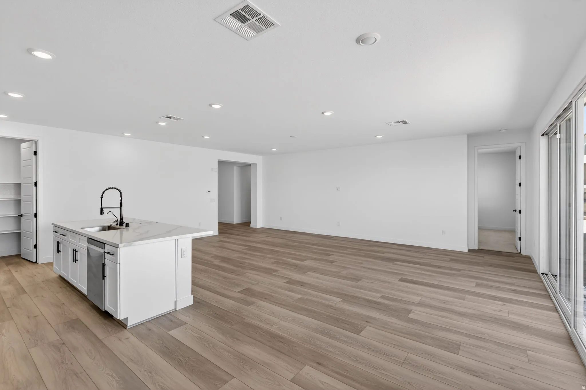 Kitchen with a kitchen island with sink, recessed lighting, white cabinets, light wood-type flooring, and light stone counters