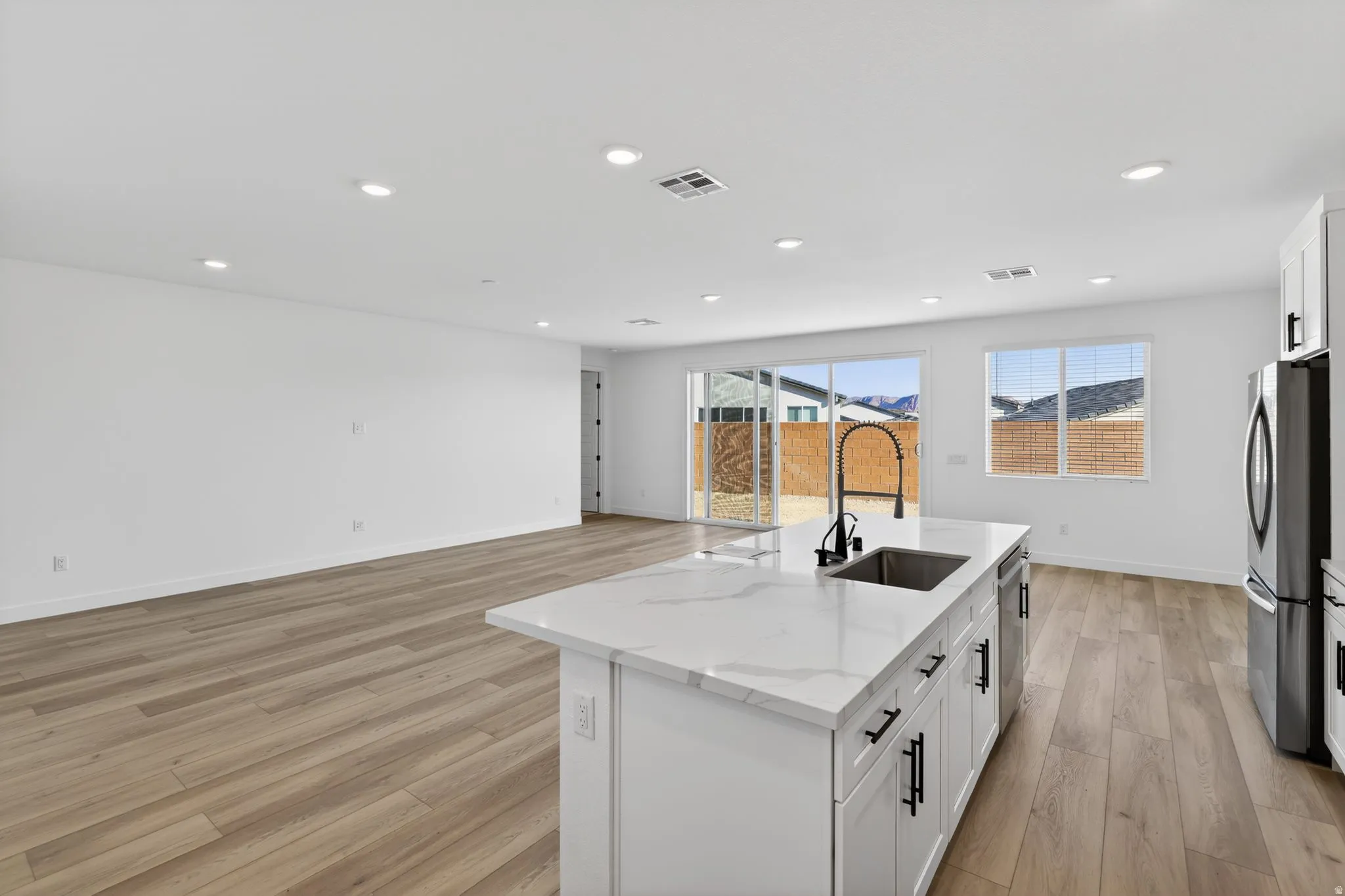 Kitchen with a center island with sink, light wood-type flooring, white cabinets, light stone countertops, and freestanding refrigerator