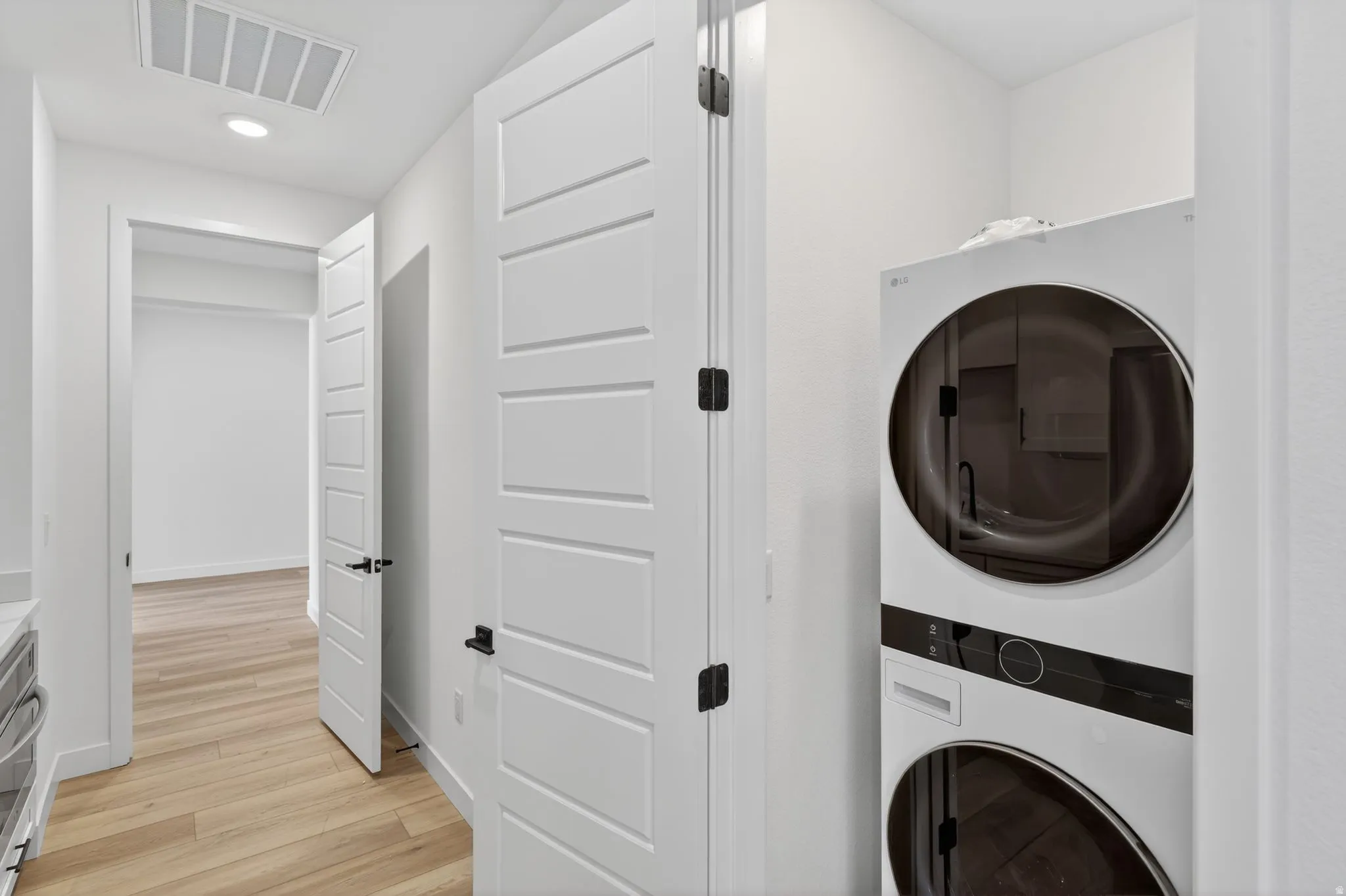 Laundry area featuring stacked washing machine and dryer, light wood-type flooring, and recessed lighting