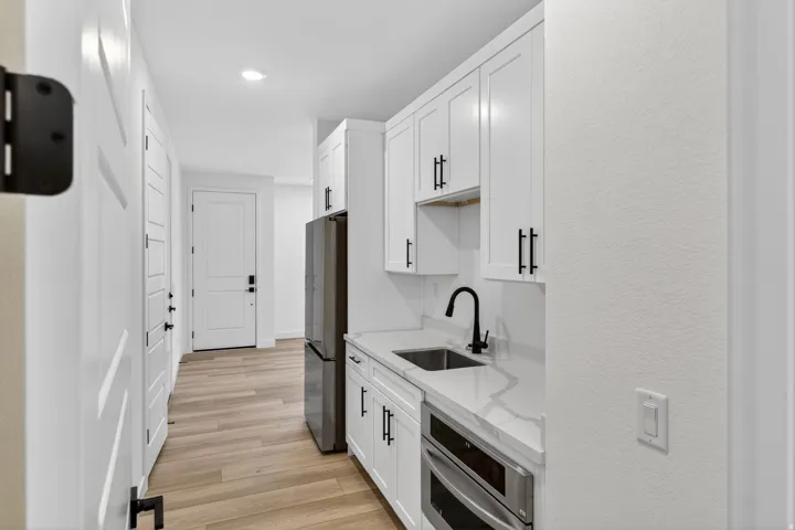 Kitchen featuring stainless steel appliances, white cabinets, light wood finished floors, light stone counters, and a textured wall