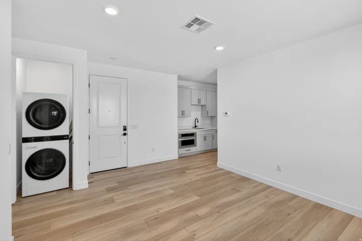 Laundry area with stacked washing machine and dryer, light wood finished floors, and recessed lighting
