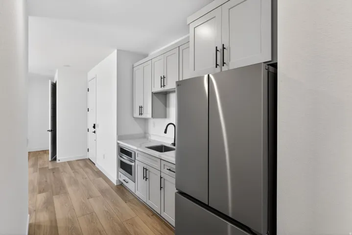 Kitchen with stainless steel appliances, light wood-style flooring, light stone counters, and white cabinetry