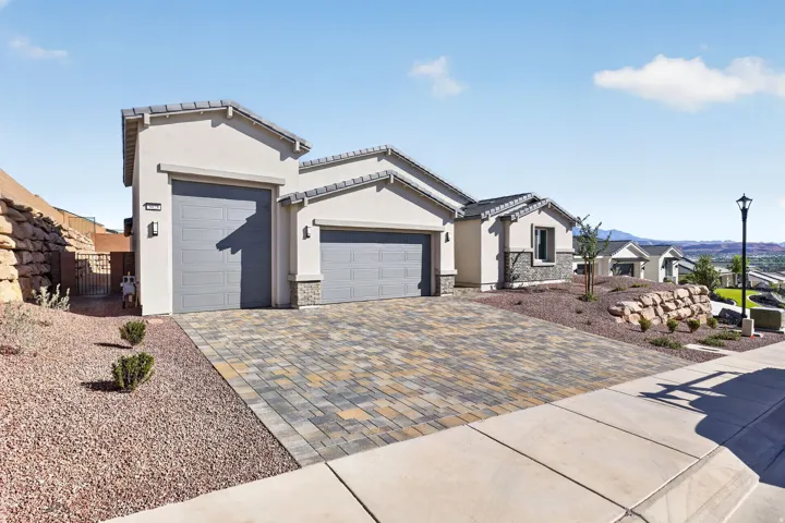 View of front of home featuring an attached garage, driveway, stucco siding, stone siding, and a tiled roof
