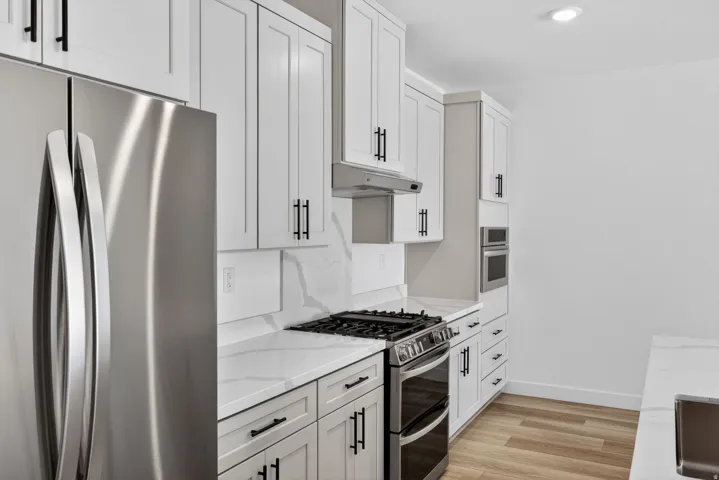 Kitchen with stainless steel appliances, light wood-type flooring, light stone countertops, and white cabinets