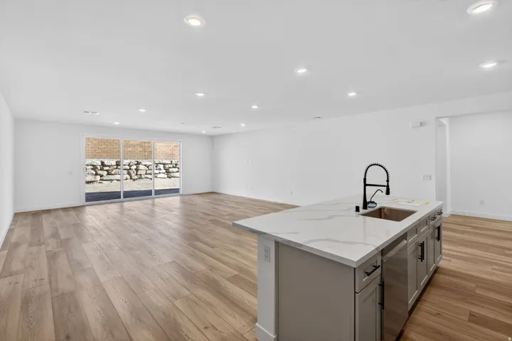 Kitchen featuring a center island with sink, light stone countertops, light wood finished floors, recessed lighting, and open floor plan