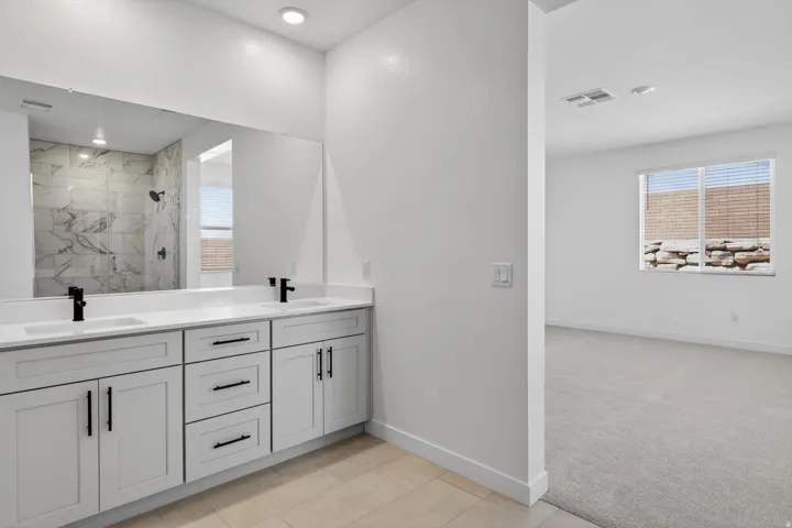 Full bath featuring a marble finish shower, double vanity, light carpet, and light tile patterned floors
