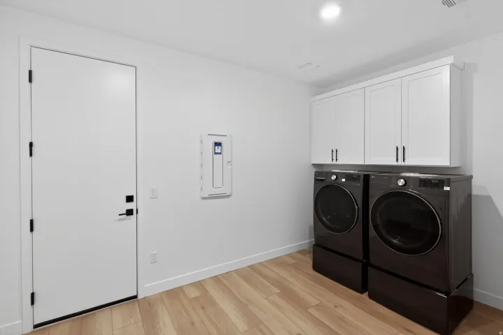 Laundry area with cabinet space, light wood-style floors, washing machine and dryer, and electric panel