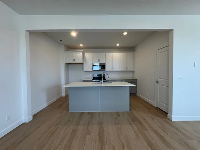 Dual tone kitchen featuring recessed lighting, light wood-style floors, a kitchen island with sink, stainless steel appliances, and light stone counters