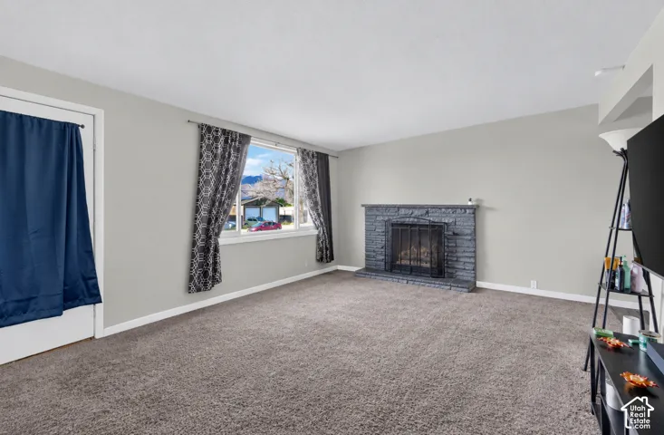 Stone-clad fireplace with hearth, carpeted flooring, and large window