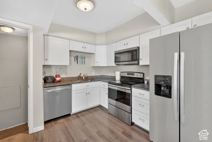 Kitchen with stainless steel appliances, white cabinetry, light wood finished floors, and dark stone countertops