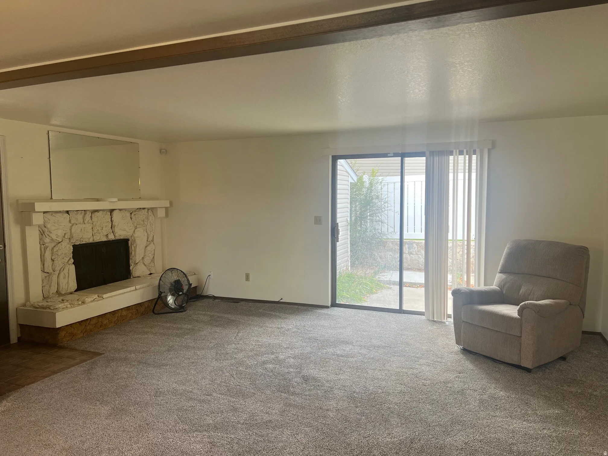 Carpeted living area with a stone fireplace and beamed ceiling