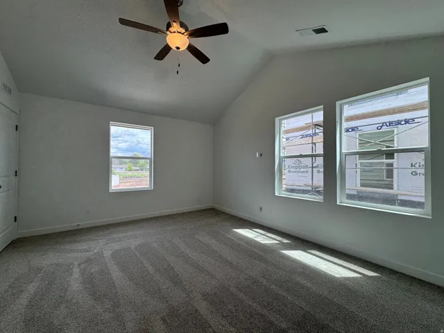 Carpeted empty room with lofted ceiling and a ceiling fan