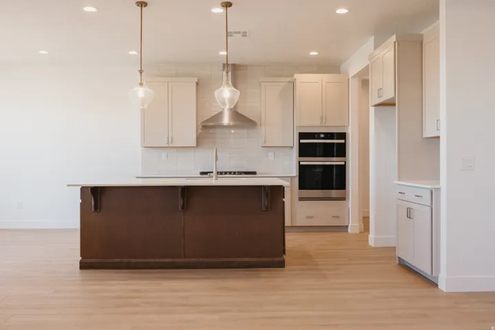 Kitchen featuring a kitchen bar, light wood-style floors, a kitchen island with sink, and double oven