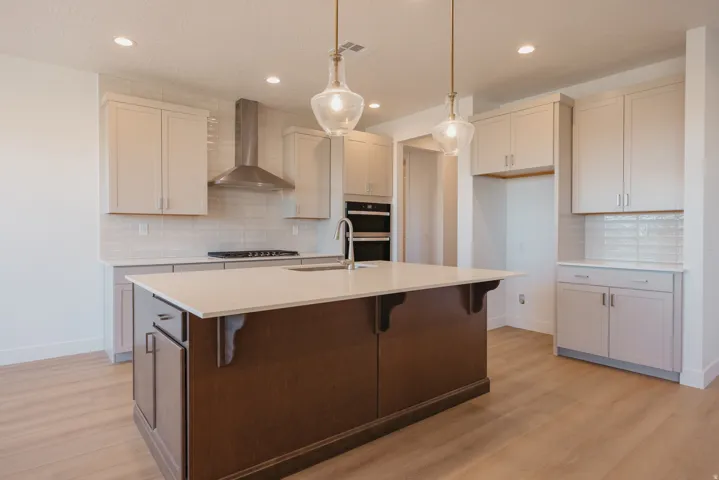 Kitchen featuring a kitchen breakfast bar, tasteful backsplash, hanging light fixtures, light wood-style floors, and an island with sink