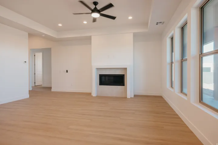 Unfurnished living room with a ceiling fan, a tray ceiling, light wood-style floors, recessed lighting, and a tiled fireplace
