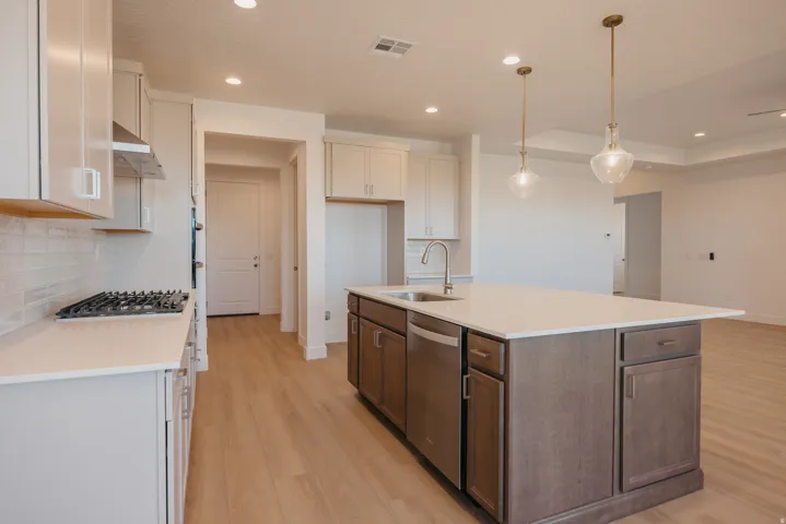 Dual tone kitchen with light wood-style flooring, a center island with sink, two tone color scheme, decorative light fixtures, and stainless steel appliances