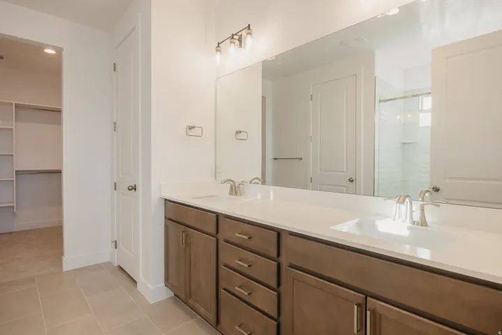 Full bath with double vanity, a shower stall, light tile patterned flooring, and a spacious closet