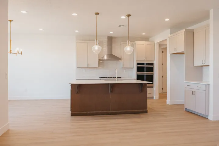 Dual tone kitchen with a breakfast bar area, light wood-style floors, an island with sink, light stone counters, and dual tone cabinets