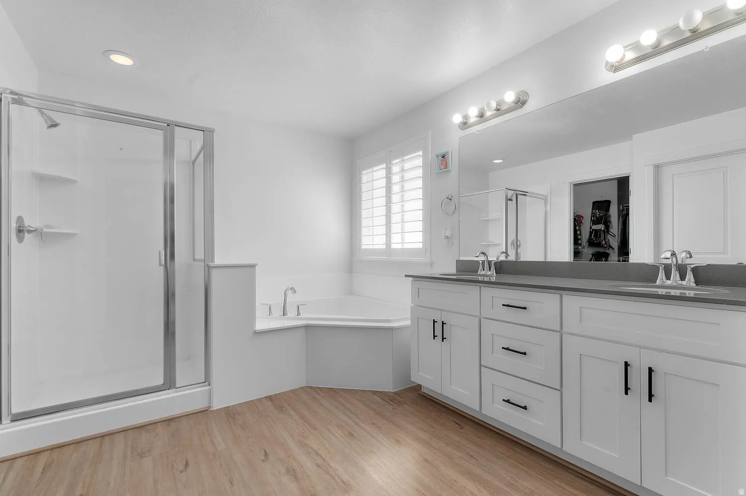 Bathroom featuring a stall shower, double vanity, light wood-style floors, a garden tub, and a walk in closet