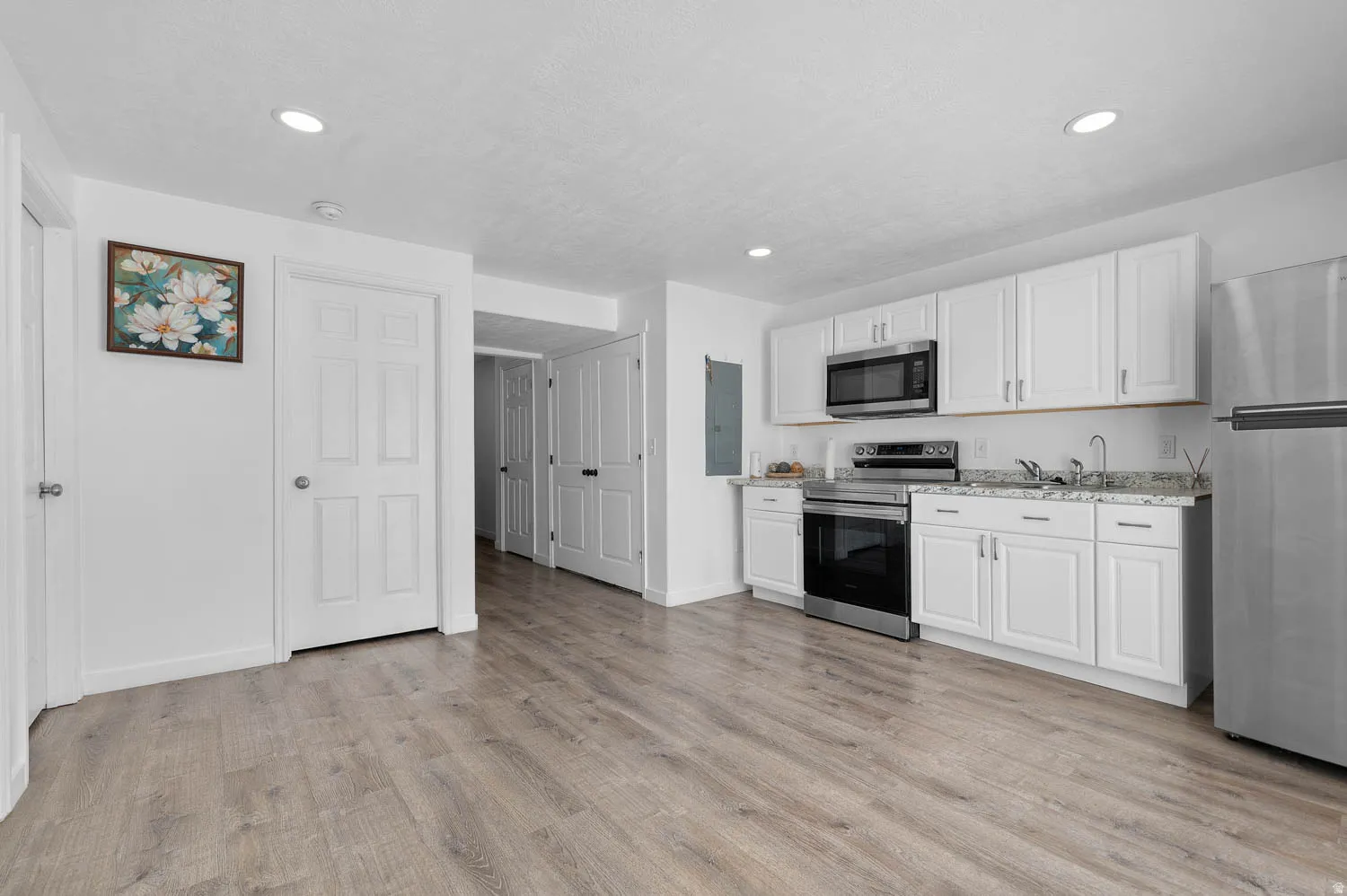 Kitchen with stainless steel appliances, white cabinets, light wood-style floors, light stone counters, and recessed lighting