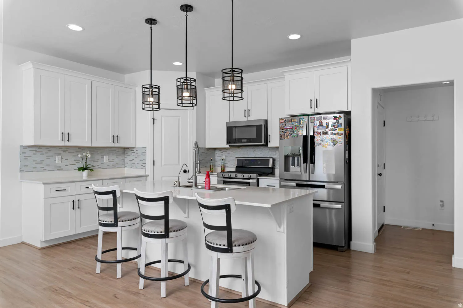 Kitchen featuring stainless steel appliances, a breakfast bar, a kitchen island with sink, white cabinets, and light wood finished floors
