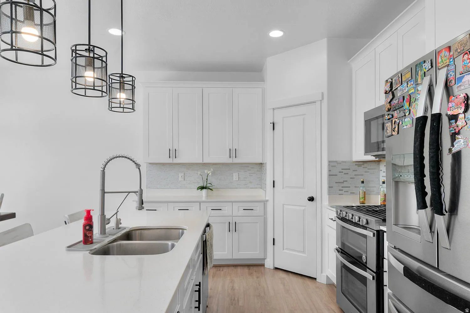 Kitchen featuring stainless steel appliances, white cabinetry, light wood-type flooring, and pendant lighting