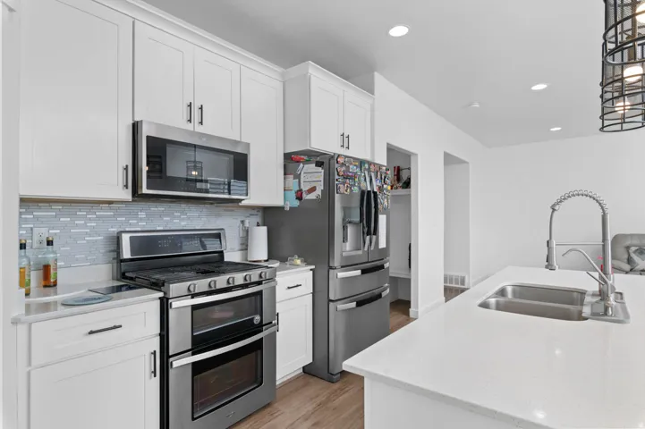 Kitchen featuring stainless steel appliances, light wood-style floors, white cabinets, light stone counters, and recessed lighting