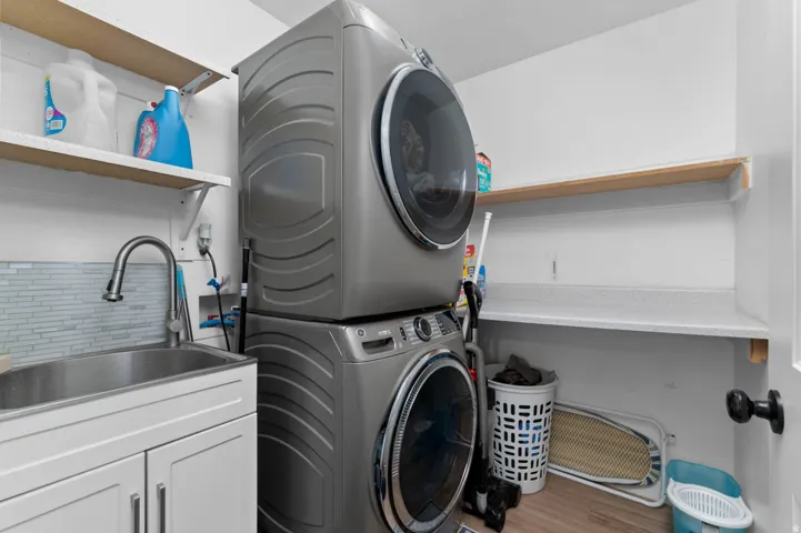 Laundry room with stacked washer / drying machine and light wood-style flooring