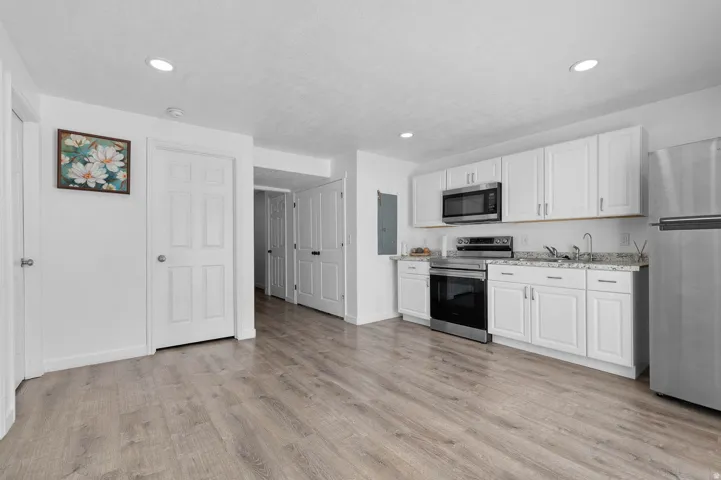Kitchen with stainless steel appliances, white cabinets, light wood-style floors, light stone counters, and recessed lighting