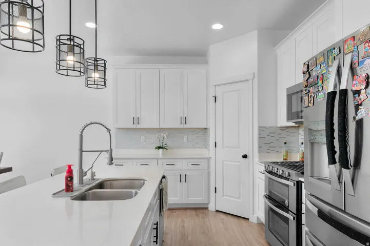 Kitchen featuring stainless steel appliances, white cabinetry, light wood-type flooring, and pendant lighting