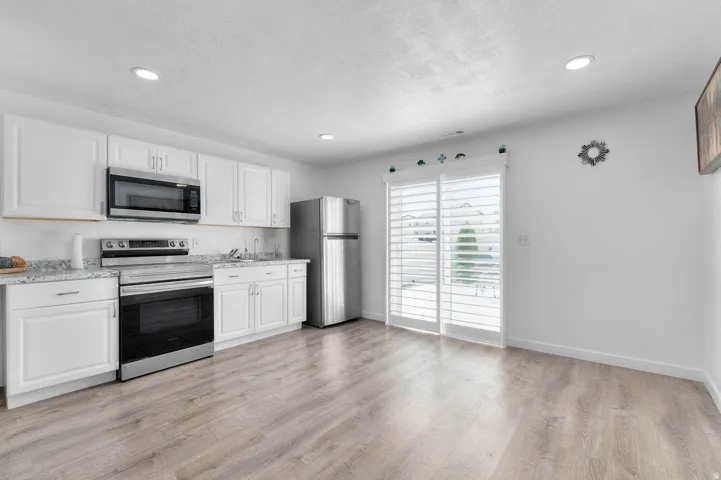 Kitchen featuring stainless steel appliances, white cabinets, recessed lighting, light wood finished floors, and light stone counters