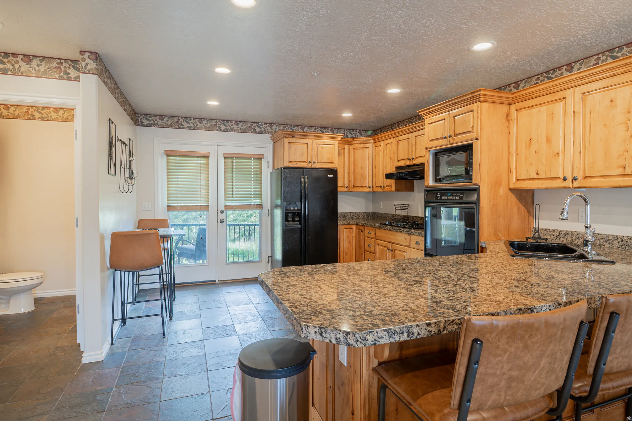 Kitchen with stone tile floors, a peninsula, black appliances, a kitchen bar, and recessed lighting