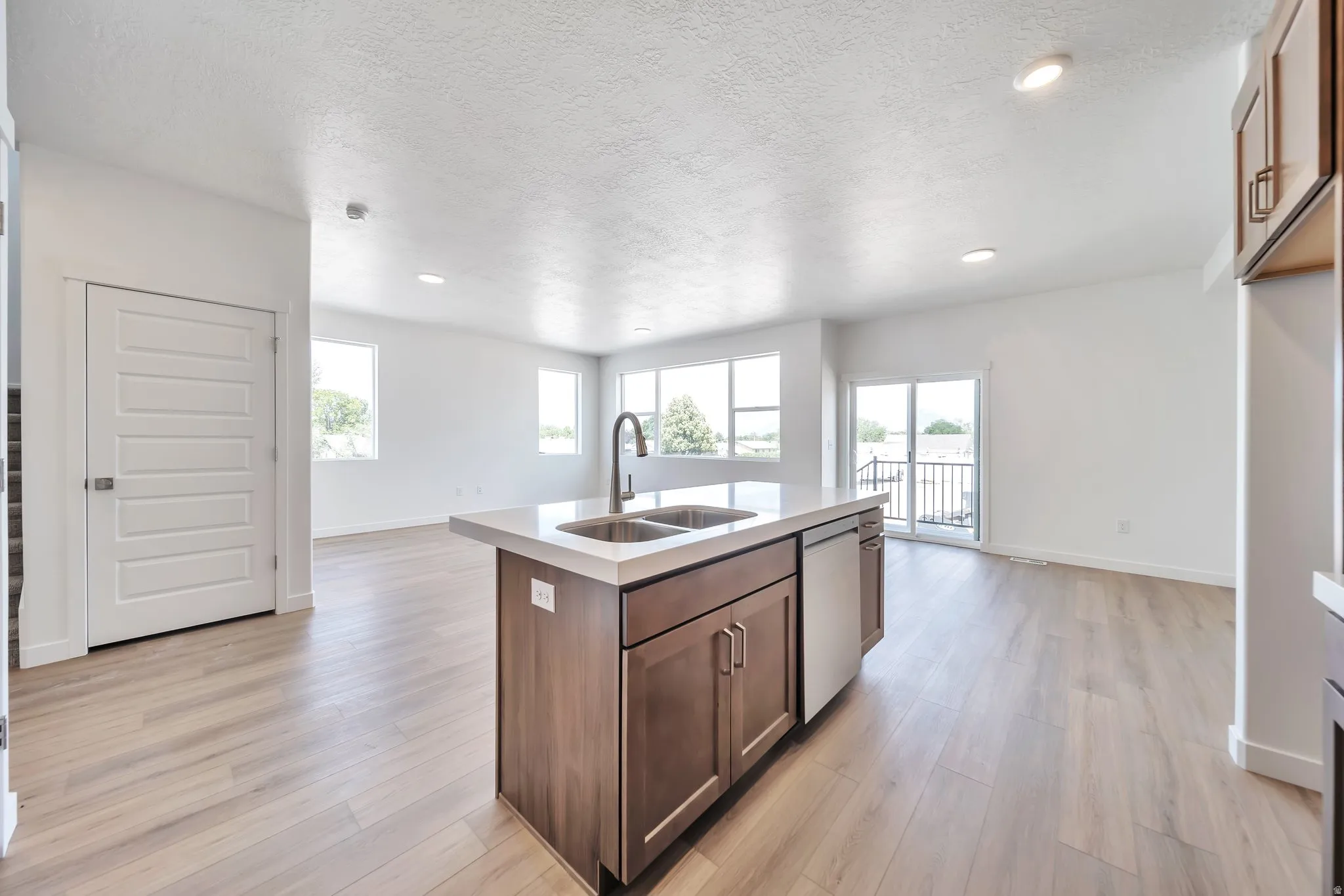 Kitchen featuring a center island with sink, open floor plan, a textured ceiling, light wood-type flooring, and healthy amount of natural light