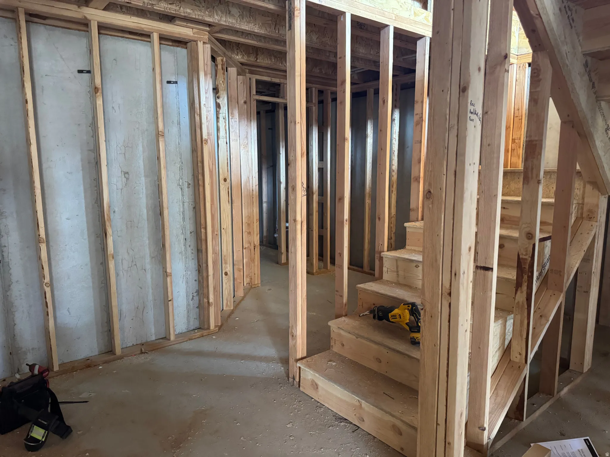 Unfinished basement space featuring exposed wood framing, concrete foundation walls, and a newly constructed wooden staircase