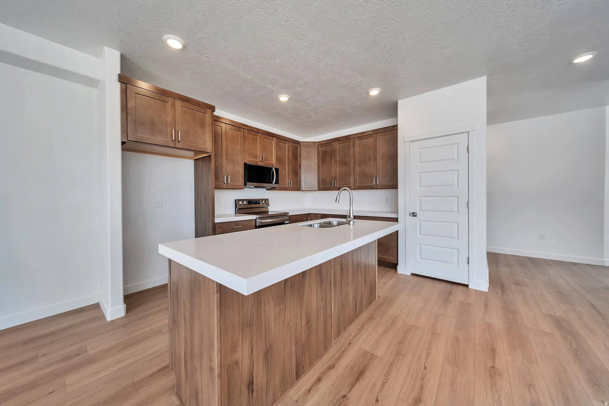 Kitchen with stainless steel appliances, light wood-style floors, a center island with sink, wood finish cabinets, and recessed lighting