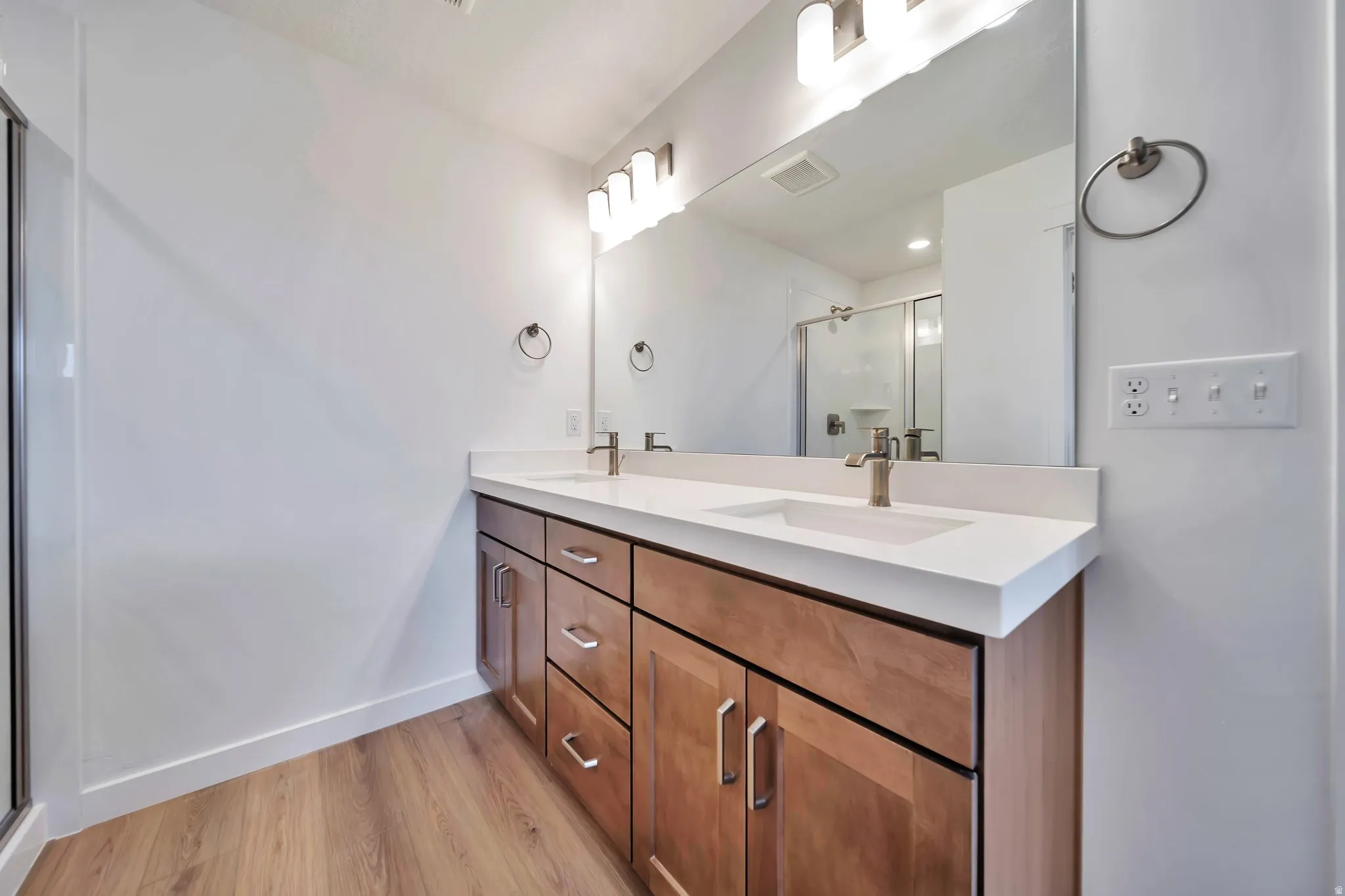 Bathroom featuring a shower stall, double vanity, and light wood-type flooring