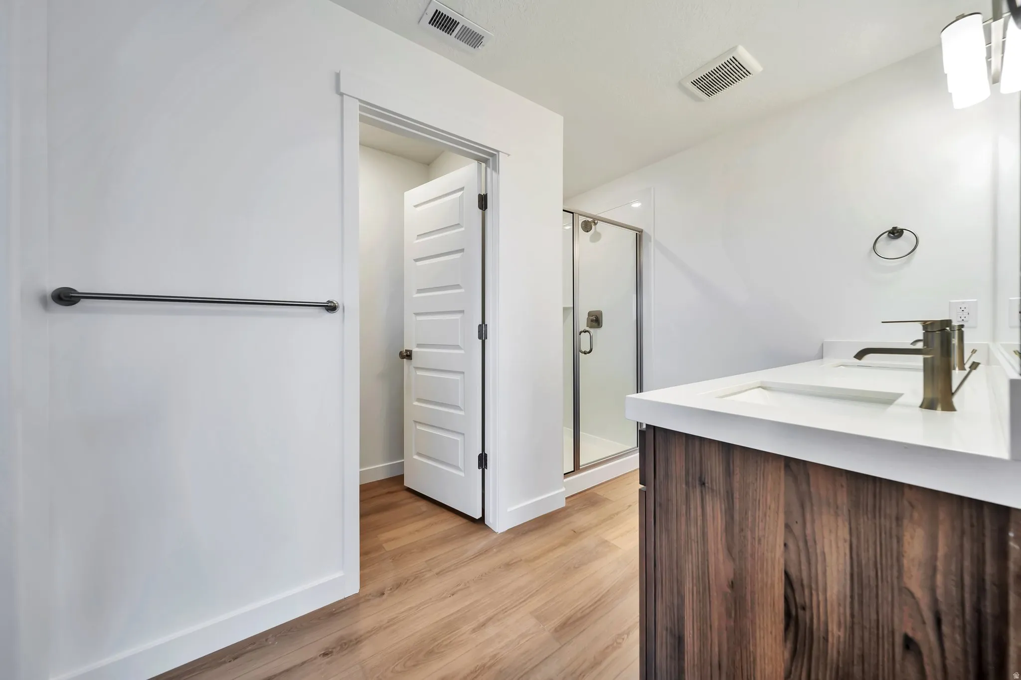 Full bath featuring a shower stall, double vanity, and light wood finished floors