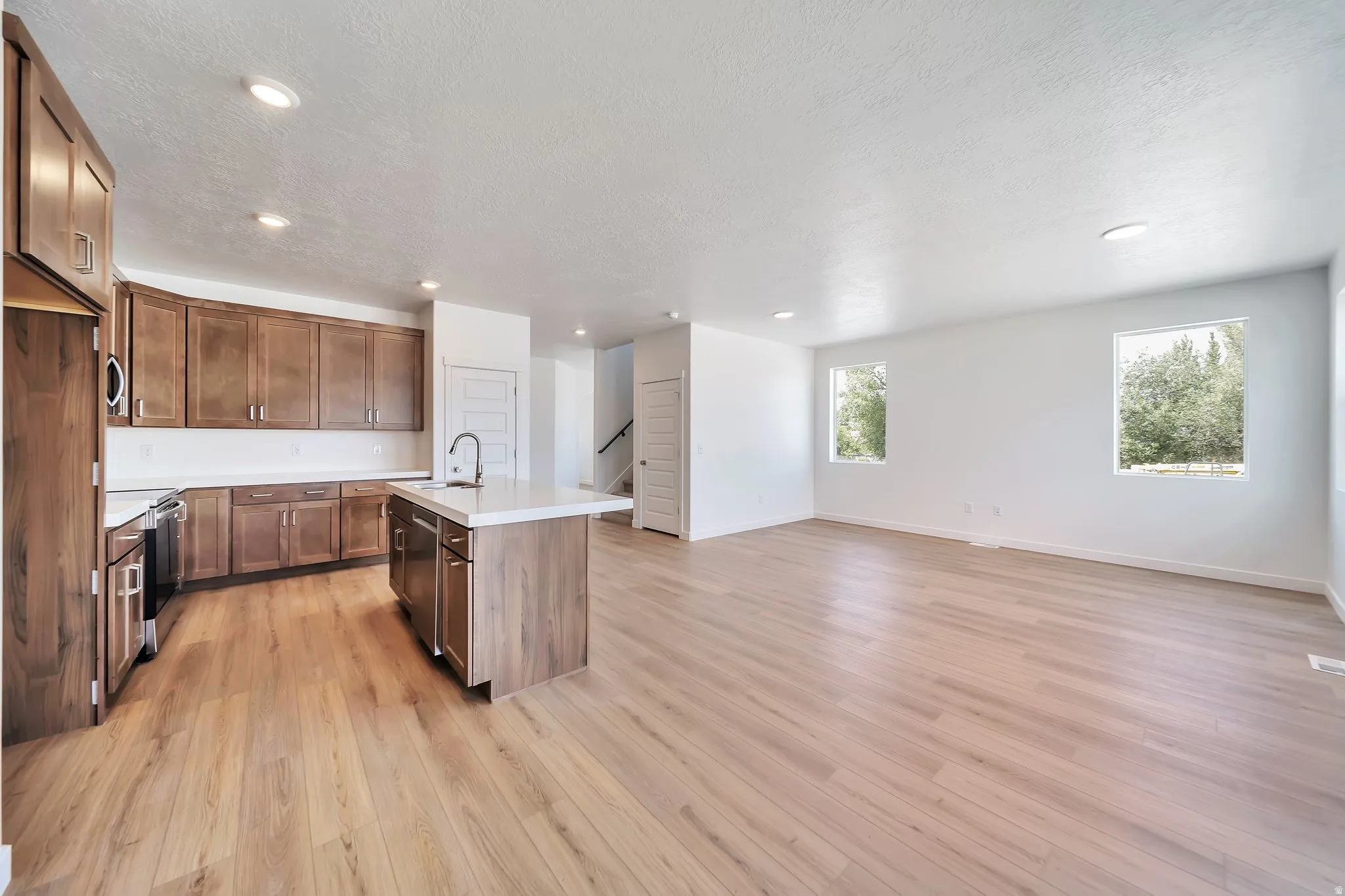 Kitchen with open floor plan, light countertops, a center island with sink, stainless steel appliances, and light wood-style floors